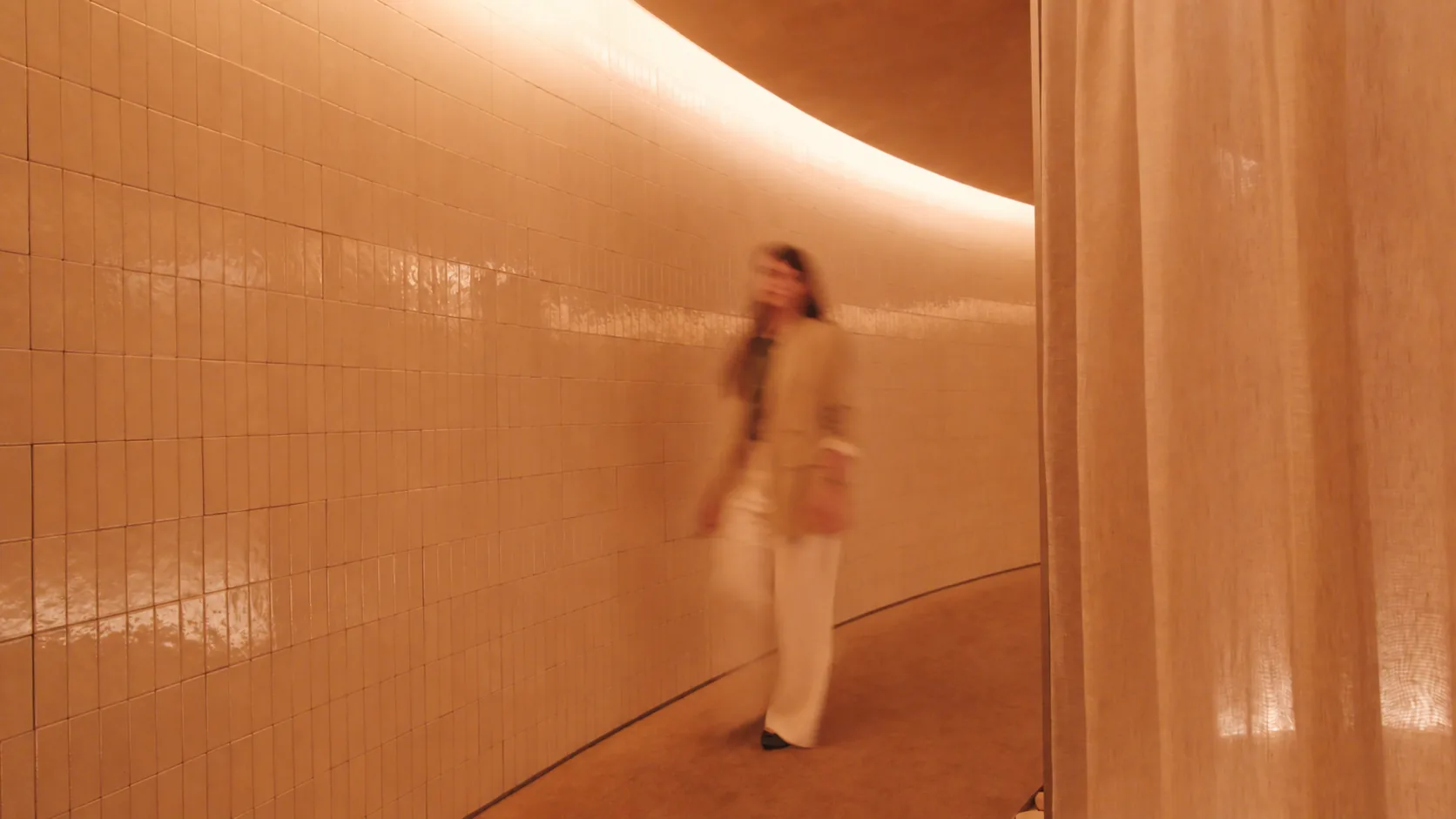 Mulher caminhando por um corredor curvo revestido de azulejos no Haikai.